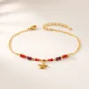 Pulseira dourada com missangas vermelhas e pendente sobre fundo claro