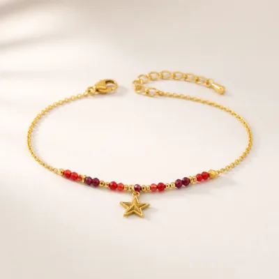 Pulseira dourada com missangas vermelhas e pendente sobre fundo claro
