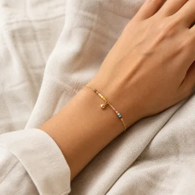 Pulseira dourada com missangas multicolores e pendente apresentada no pulso
