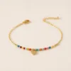 Pulseira dourada com missangas multicolores e pendente sobre fundo claro