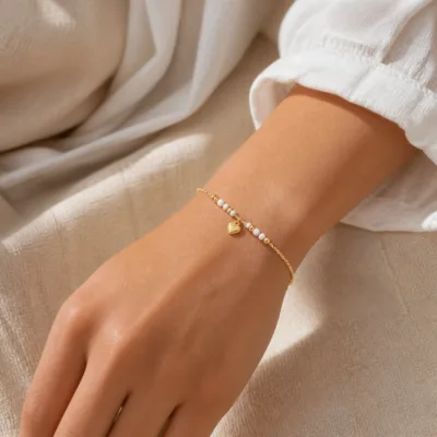 Pulseira dourada com missangas brancas, pérola e pendente apresentada no pulso