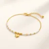 Pulseira dourada com missangas brancas, pérola e pendente sobre fundo claro