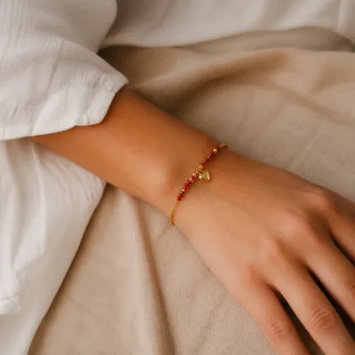 Pulseira dourada com missangas vermelhas, contas bordô e pendente apresentada no pulso