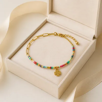 Pulseira dourada com missangas multicolores, elos ovais e pendente de trevo em caixa de joalharia