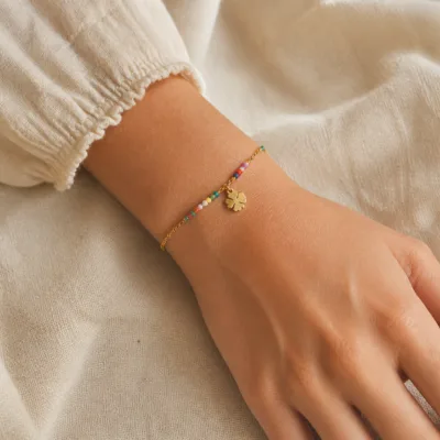 Pulseira dourada com missangas multicolores, elos ovais e pendente de trevo apresentada no pulso