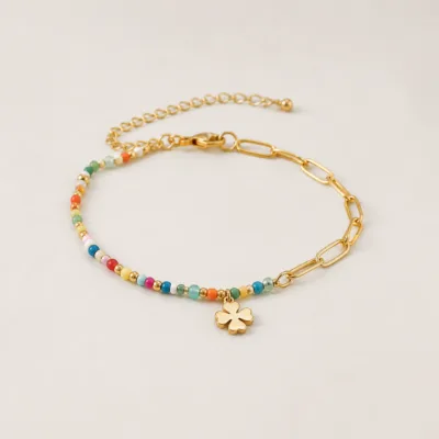 Pulseira dourada com missangas multicolores, elos ovais e pendente de trevo sobre fundo claro