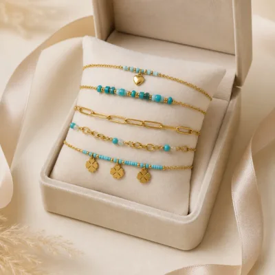 Pulseira dourada com missangas azul-claro e turquesa, elos ovais e pendente de trevo em caixa de joalharia