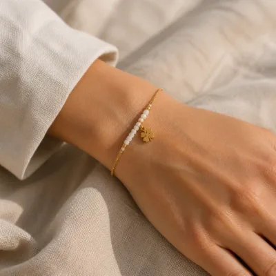 Pulseira dourada branca com pendente de trevo apresentada no pulso