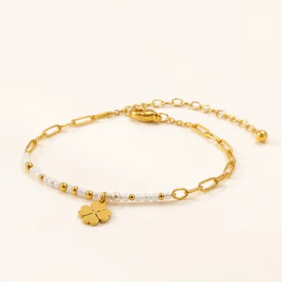 Pulseira dourada branca com pendente de trevo sobre fundo claro