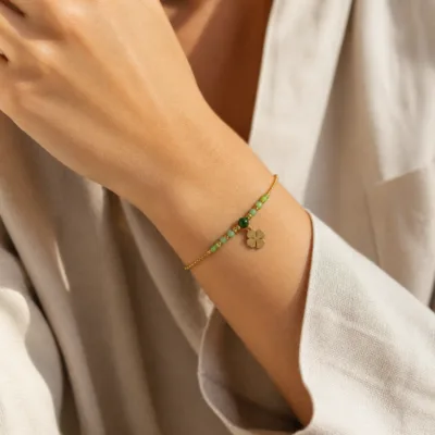 Pulseira dourada com missangas verdes, elos ovais e pendente de trevo apresentada no pulso