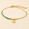 Pulseira dourada com missangas verdes, elos ovais e pendente de trevo sobre fundo claro