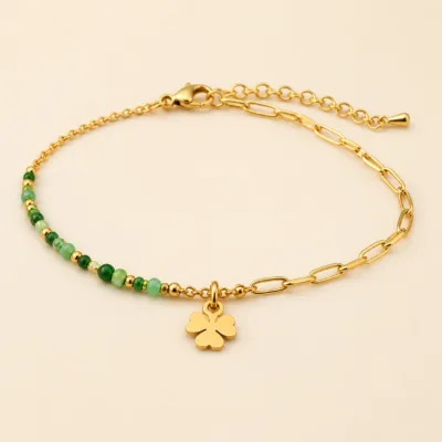 Pulseira dourada com missangas verdes, elos ovais e pendente de trevo sobre fundo claro