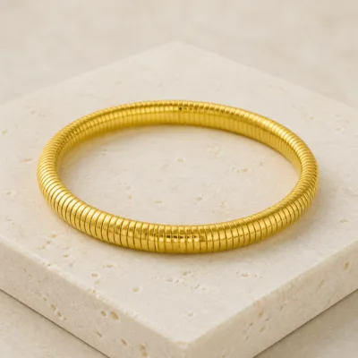 Pulseira dourada canelada sobre pedra clara