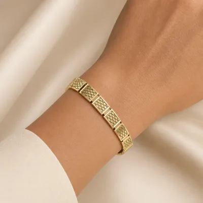 Pulseira dourada com padrão de losangos usada no pulso