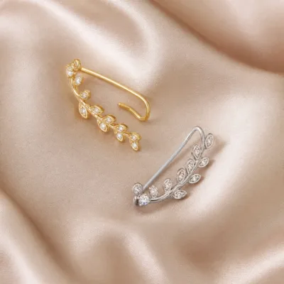 Ear cuffs dourado e prateado com folhas e cristais sobre seda neutra