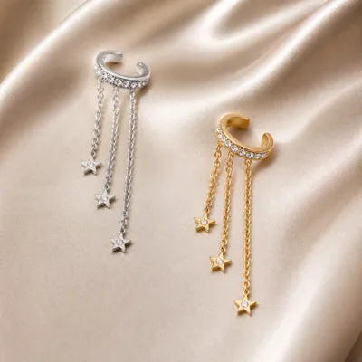 Ear cuffs prateado e dourado com estrelas sobre seda neutra