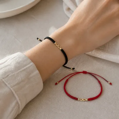 Pulseira preta com infinito dourado no pulso e variante vermelha