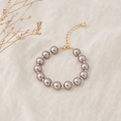 Pulseira dourada de pérolas cinza-taupe em composição editorial