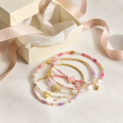 Pulseira dourada com missangas rosa, lilás e brancas em caixa de joalharia