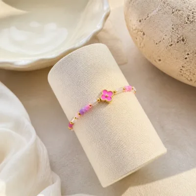 Pulseira dourada com missangas rosa, lilás e brancas apresentada em contexto de uso