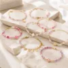 Pulseira dourada com missangas rosa, lilás e brancas sobre fundo claro