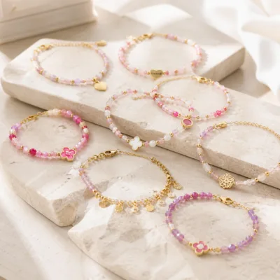 Pulseira dourada com missangas rosa, lilás e brancas sobre fundo claro