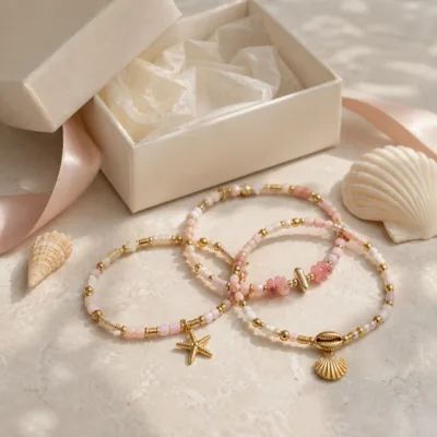 Pulseira dourada com missangas rosa e brancas com motivos marinhos em caixa de joalharia