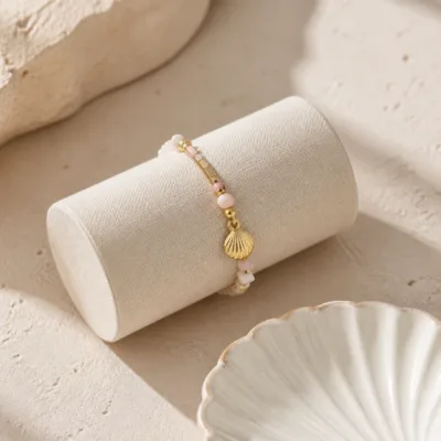 Pulseira dourada com missangas rosa e brancas com motivos marinhos apresentada em contexto de uso