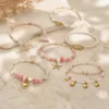 Pulseira dourada com missangas rosa e brancas com motivos marinhos sobre fundo claro