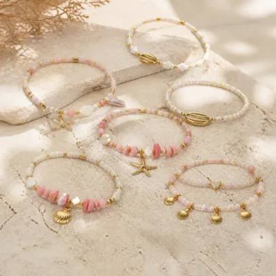 Pulseira dourada com missangas rosa e brancas com motivos marinhos sobre fundo claro