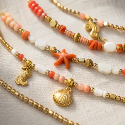 Pormenor das missangas coral, pêssego e brancas com motivos marinhos e do pendente dourado