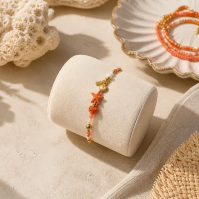 Pulseira dourada com missangas coral, pêssego e brancas com motivos marinhos apresentada em contexto de uso