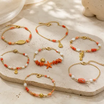 Pulseira dourada com missangas coral, pêssego e brancas com motivos marinhos sobre fundo claro