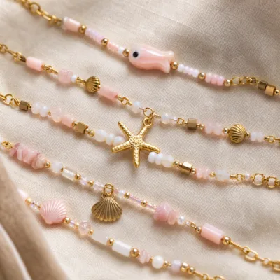 Pormenor das missangas rosa-claro e brancas com motivos marinhos e do pendente dourado