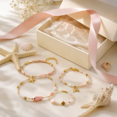 Pulseira dourada com missangas rosa-claro e brancas com motivos marinhos em caixa de joalharia