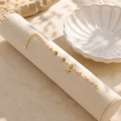 Pulseira dourada com missangas rosa-claro e brancas com motivos marinhos apresentada em contexto de uso