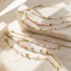 Pulseira dourada com missangas rosa-claro e brancas com motivos marinhos sobre fundo claro