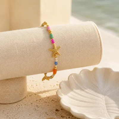 Pulseira dourada com missangas multicolores com motivos marinhos apresentada em contexto de uso