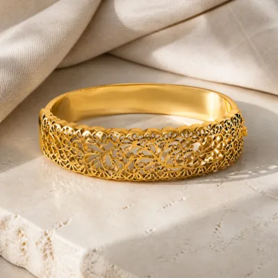 Bracelete dourado com motivos vegetais sobre linho