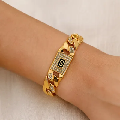 Bracelete dourado de elos com placa S usado no pulso