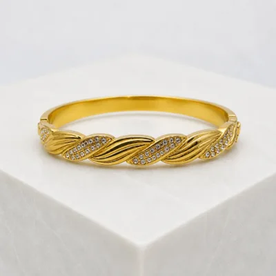Bracelete dourado entrançado sobre pedestal claro