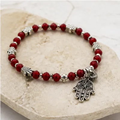 Pulseira vermelha de cristais com mão da sorte sobre pedra clara